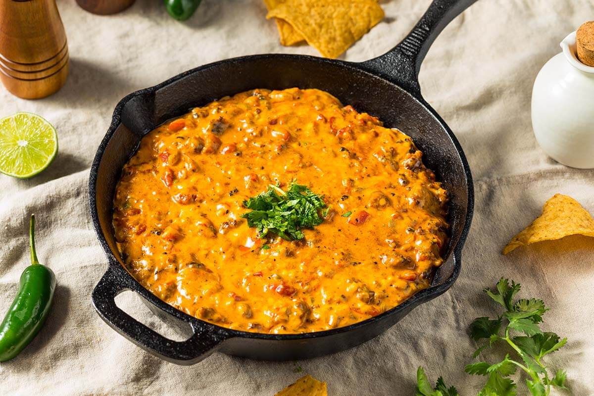 Creamy smoked queso dip in a bowl with tortilla chips on a wooden table.